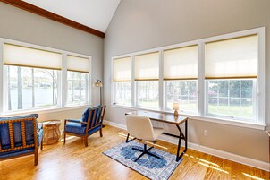 Una habitación con piso de madera, un escritorio con silla, un sillón azul y ventanas amplias con persianas.