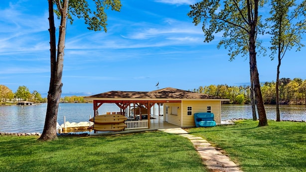 Una cabaña junto al lago con un balcón, un porche cubierto y una fuente de agua.