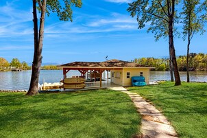 Una cabaña junto al lago con un balcón, un porche cubierto y una fuente de agua.