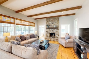 A spacious living room with a stone fireplace, wooden beams, and a large television. - Lakefront Home With Private Dock, Kayaks, Beach, Badminton, Firepit, & Deck (Mineral)