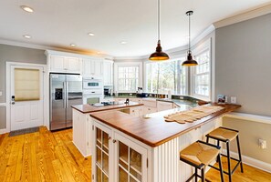 A kitchen with white cabinets, a wooden island, and a large window. - Lakefront Home With Private Dock, Kayaks, Beach, Badminton, Firepit, & Deck (Mineral)