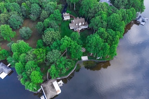 An aerial view of a lakeside property with a large house, a dock, and surrounding dense greenery. - Lakefront Home With Private Dock, Kayaks, Beach, Badminton, Firepit, & Deck (Mineral)