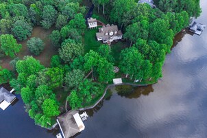 Vista aérea de una propiedad junto al lago, con una casa grande, un muelle y abundante vegetación alrededor.