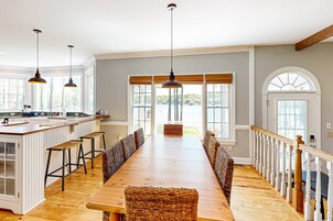 Un comedor amplio con una larga mesa de madera, techos altos y ventanas grandes.