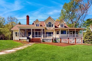 A large, two-story house with a covered porch, a chimney, and a well-maintained lawn. - Lakefront Home With Private Dock, Kayaks, Beach, Badminton, Firepit, & Deck (Mineral)
