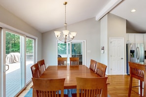 A dining area with a large wooden table and chairs, a chandelier, and a sliding glass door leading to an outdoor deck. - Exquisite Dog-friendly Home With Kayaks, Pool Table, hot Tub, & Washer/dryer (Bumpass)
