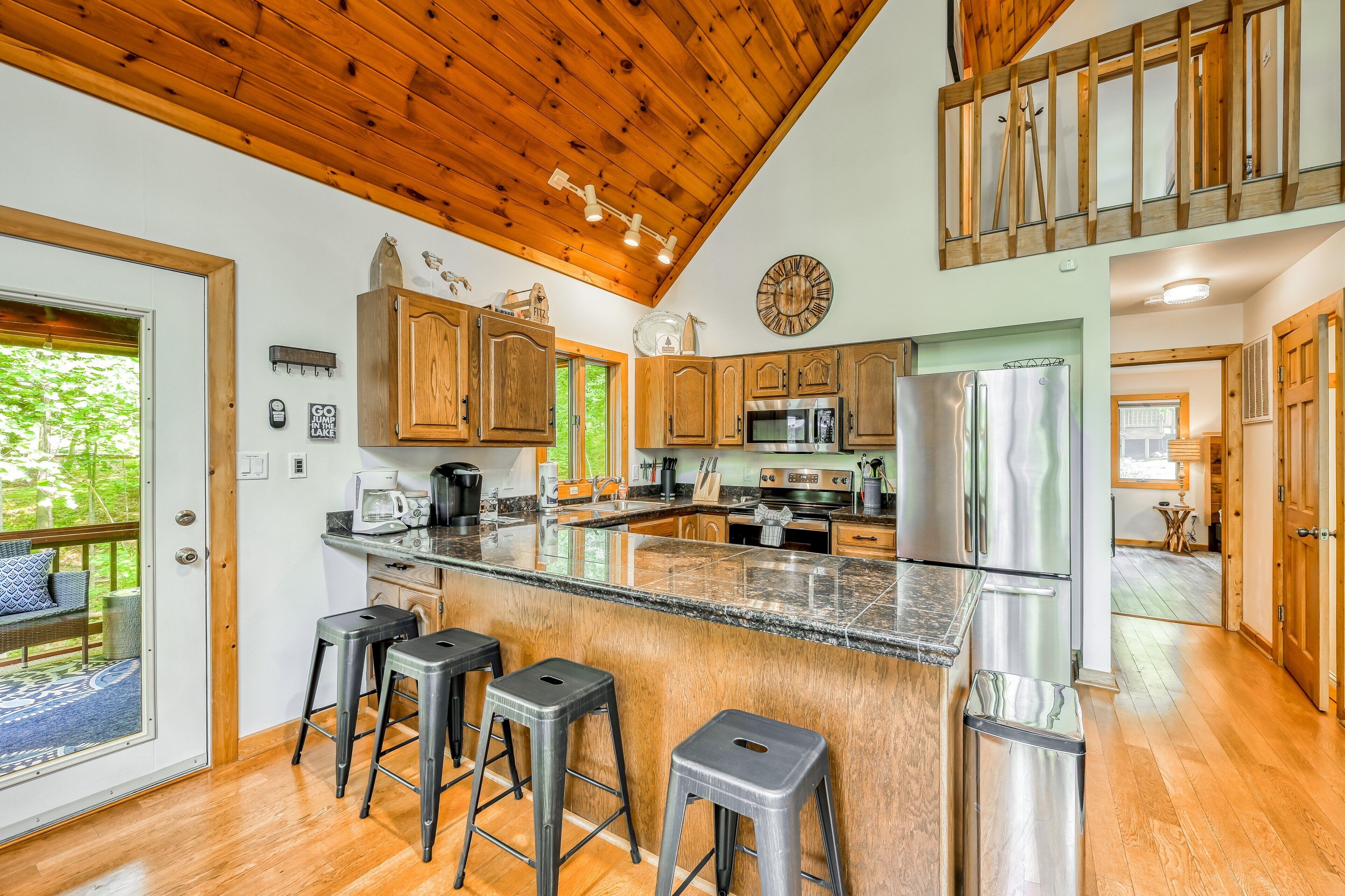 A kitchen with wooden cabinets, a stainless steel refrigerator, and a bar area with stools.