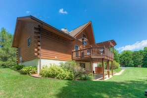 A log cabin with a balcony, surrounded by a well-maintained lawn and trees. - Three-story Dog-friendly Home With Large Deck, Wood Swing, Firepit, Lawn, & More (Mineral)