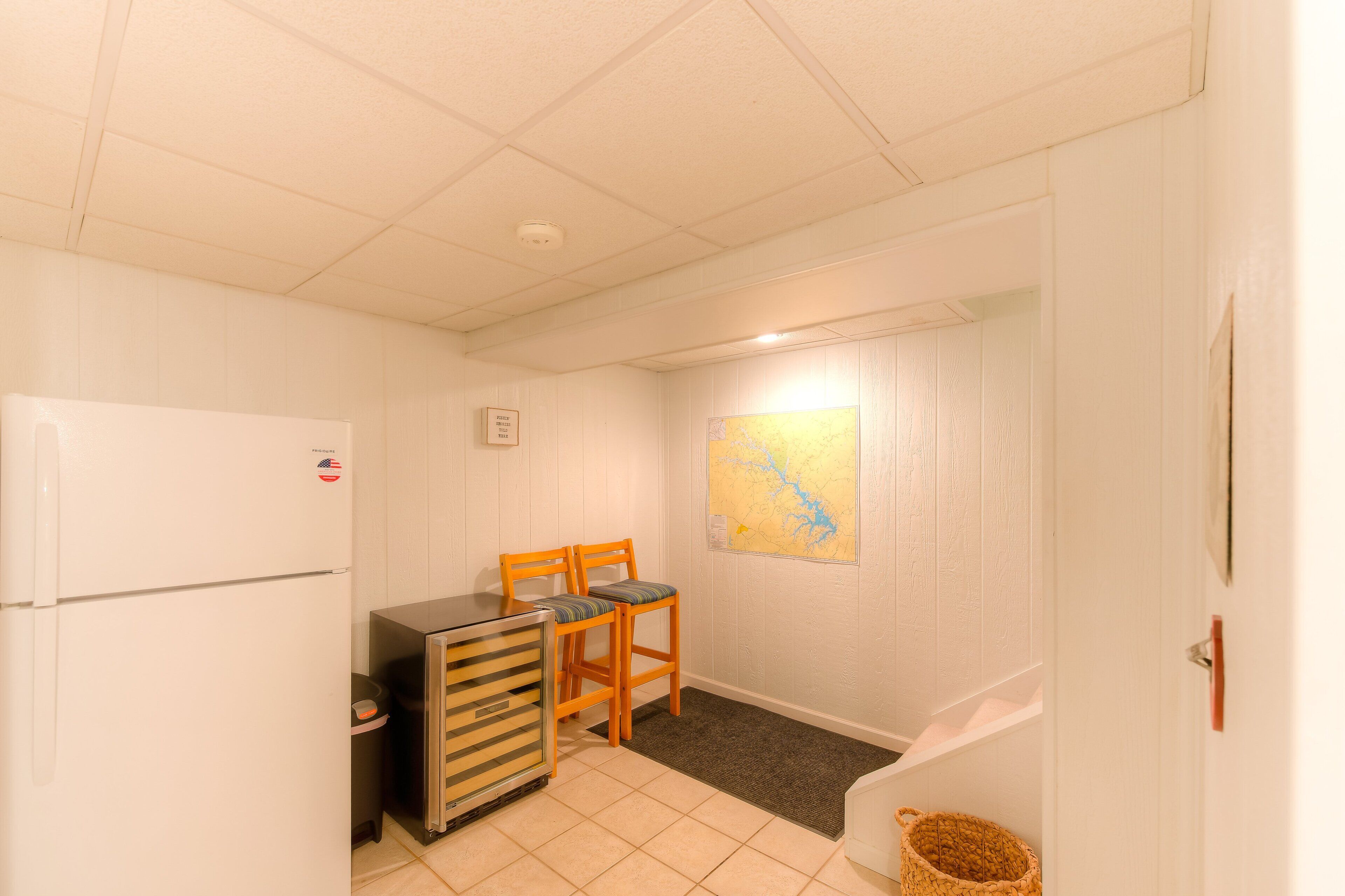 Eine kleine Küche mit Kühlschrank, einem Tisch, zwei Stühlen, einer Karte an der Wand und einer Tür zu einem weiteren Raum.