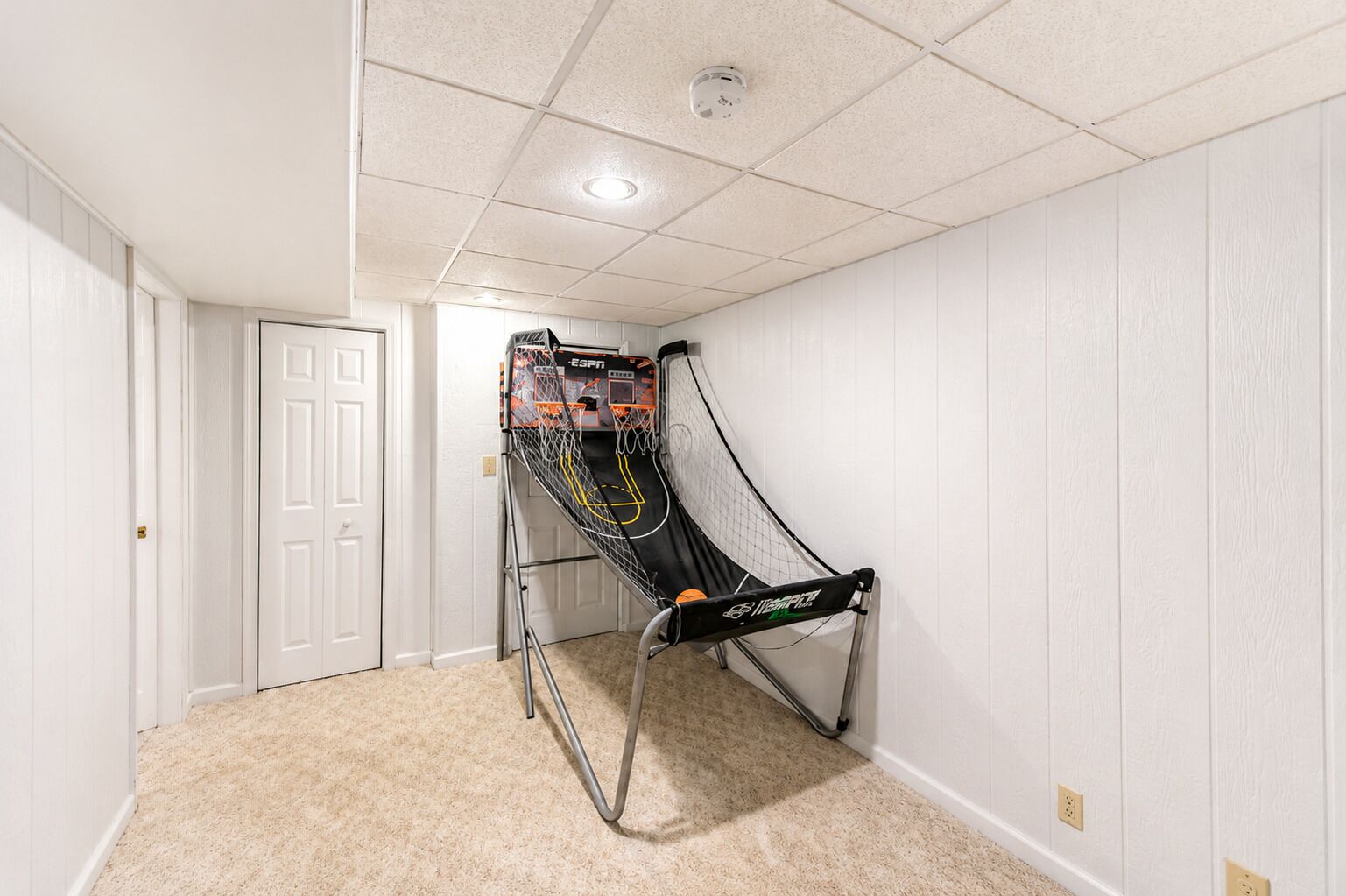A room with a basketball hoop, carpeted floor, white walls, and a door.