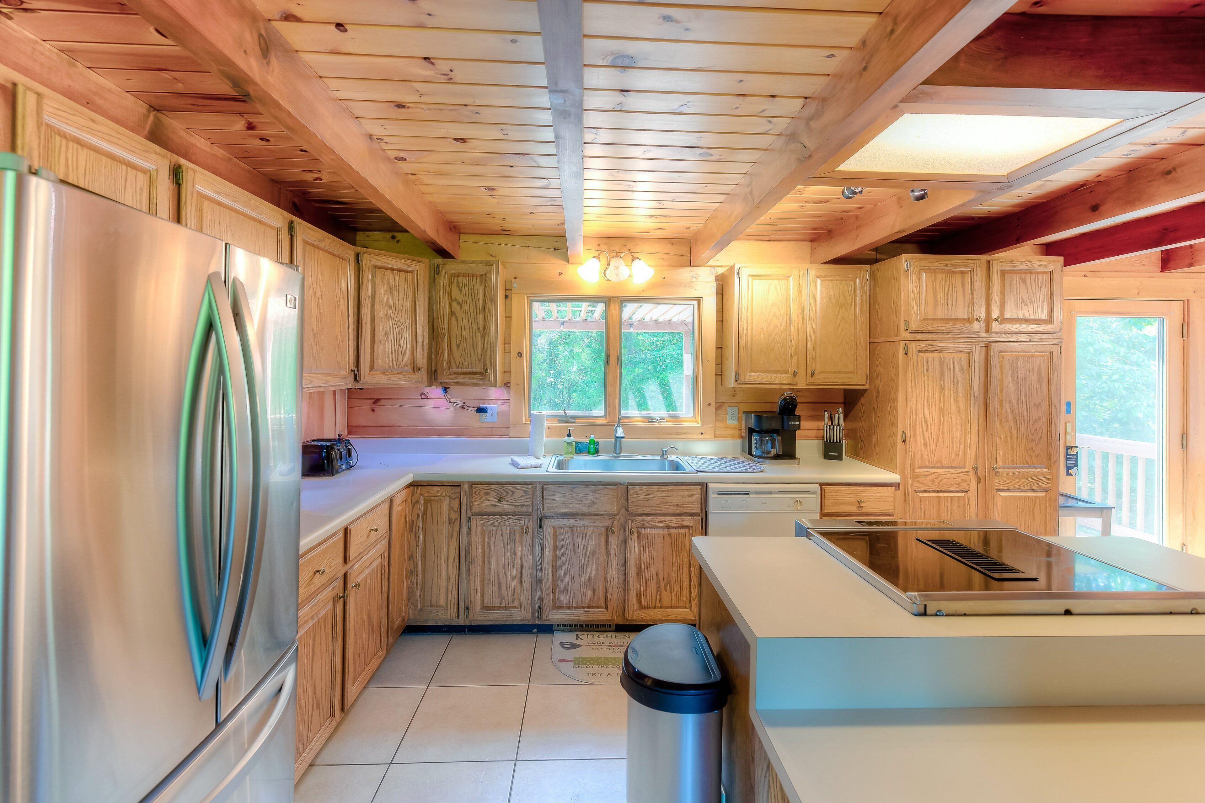 A kitchen with wooden cabinets, a stainless steel refrigerator, a sink, and a window.
