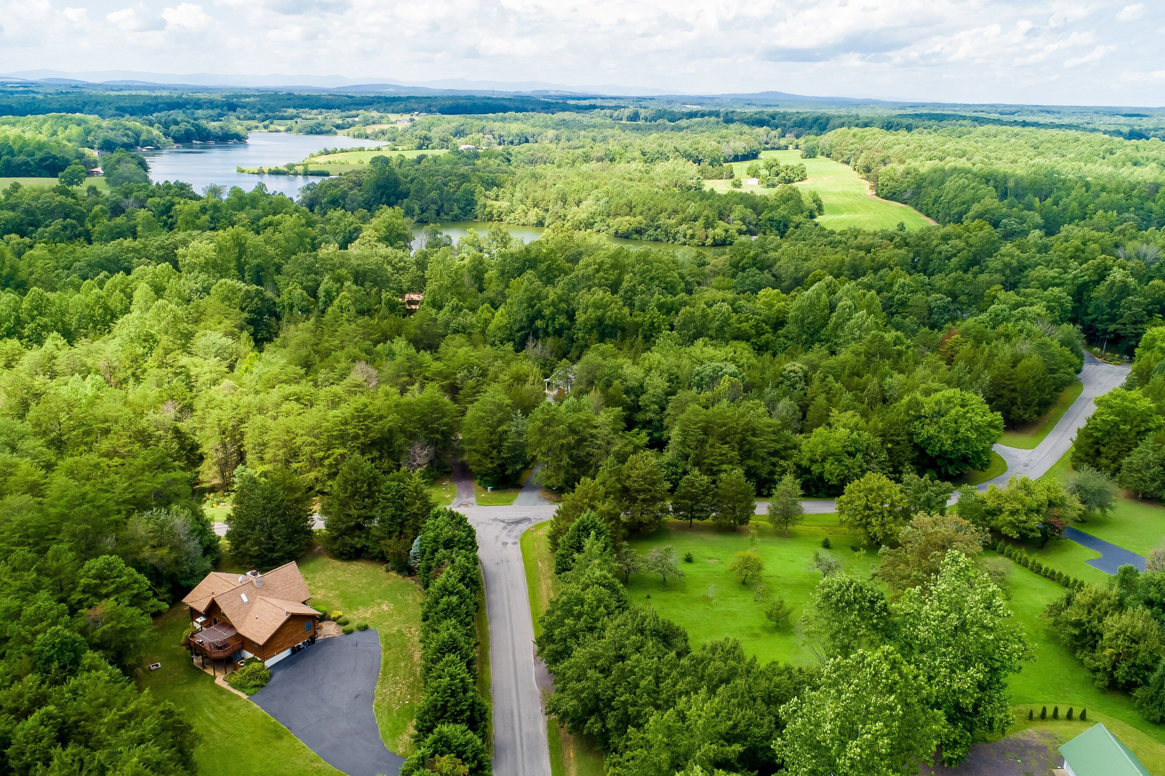 A large house surrounded by dense greenery, a golf course, and a lake.