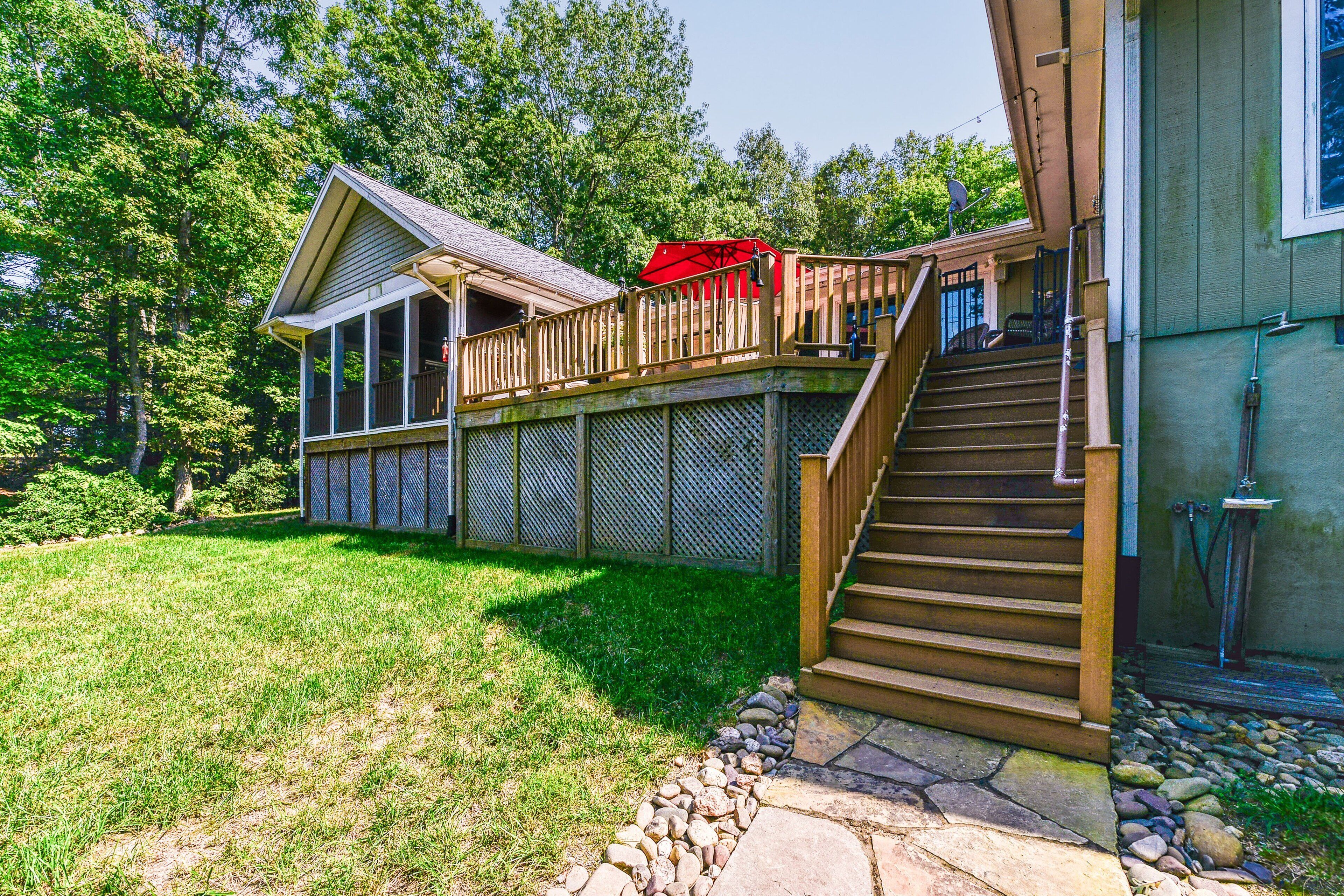 A house with a wooden deck, a staircase leading to a second floor, and a fenced backyard.