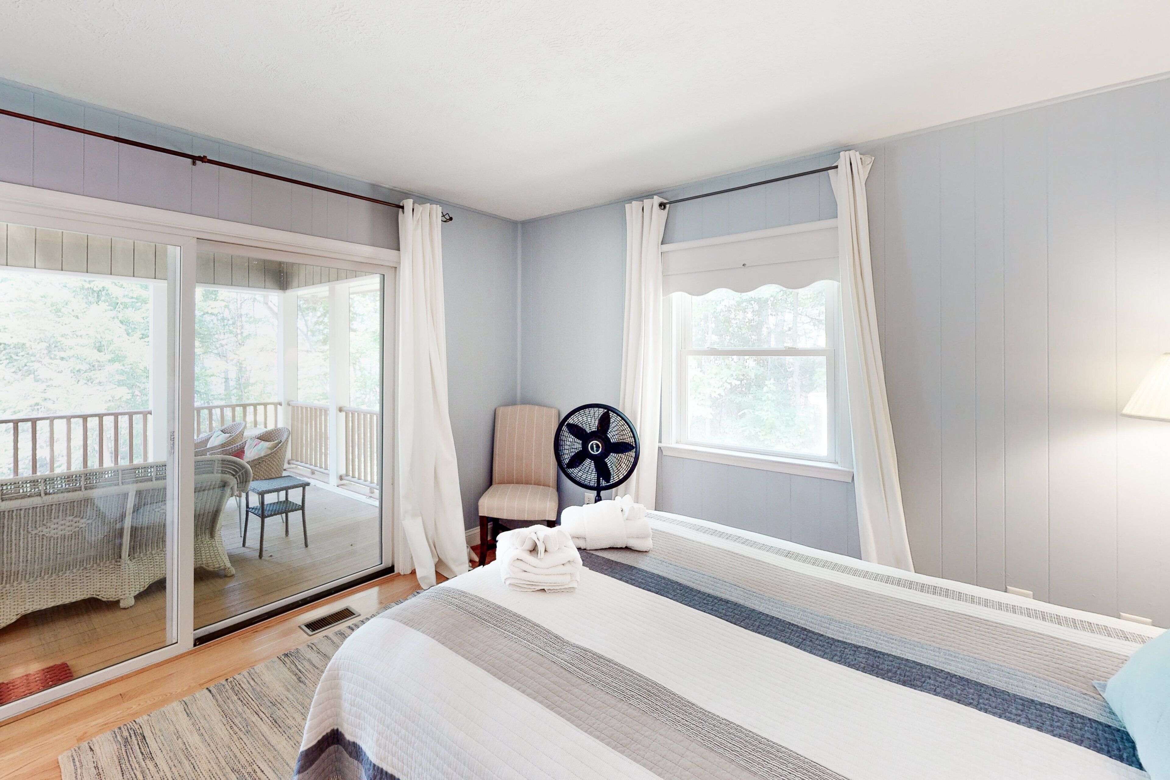 A bedroom with a bed, a chair, a fan, and a view of an outdoor balcony.