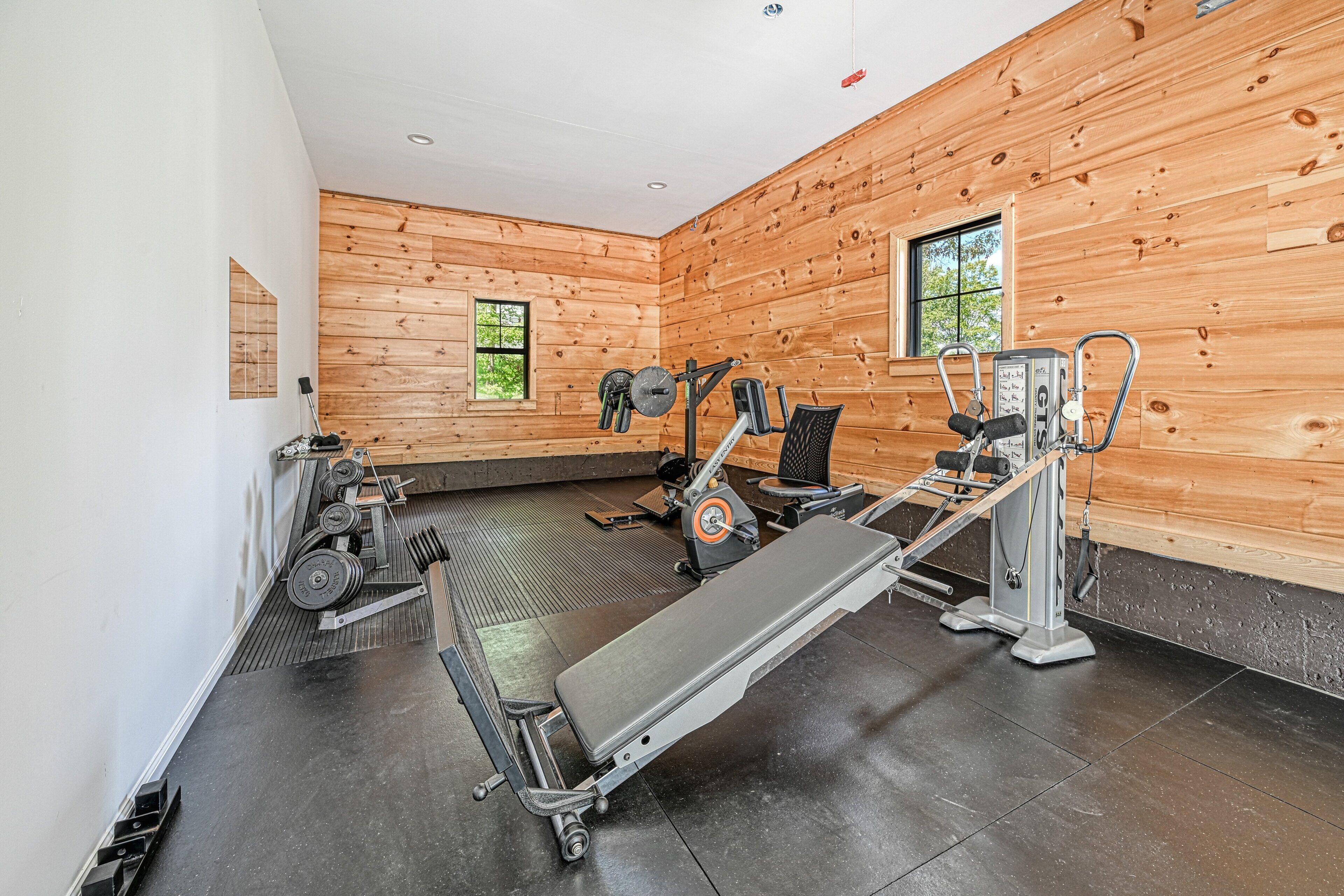 A gym with exercise equipment, wooden walls, and a window.