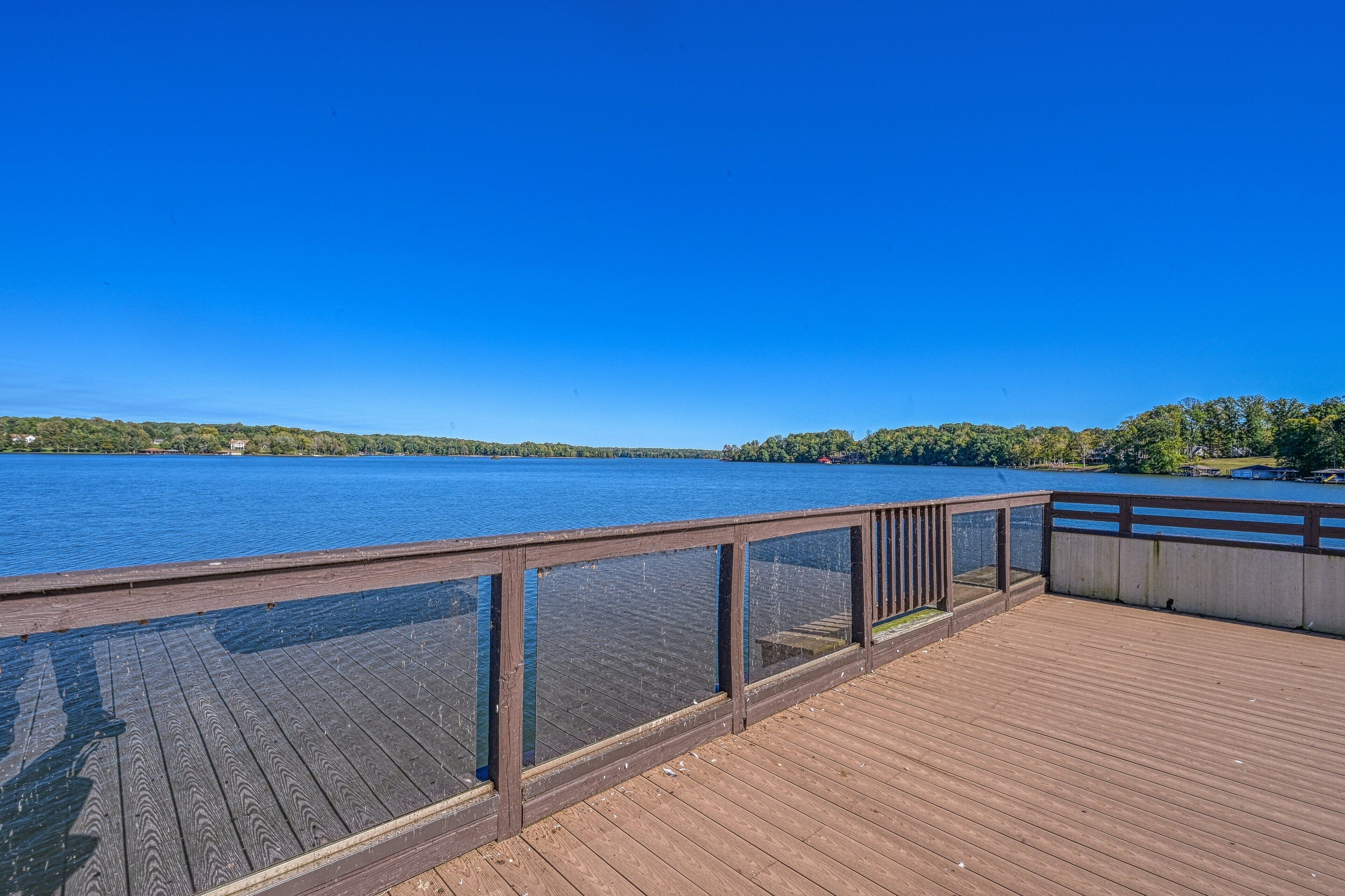 Ein Holzdeck mit Glasgeländer mit Blick auf einen ruhigen See.
