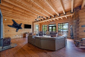 Ein Holzblockhaus-Interieur mit einem großen Ecksofa, Holzdielen und einem Kamin aus Stein.