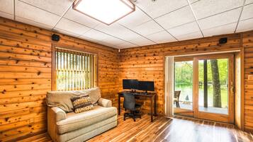A room with wooden walls, a sofa, a desk with a computer, and a sliding glass door to an outdoor area.