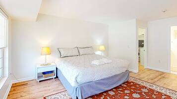 A bedroom with a bed, bedside lamps, a nightstand, a patterned rug, and a window.