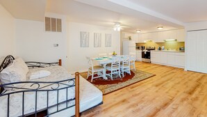 A bedroom with a bed, a dining table with chairs, a kitchen area, and a ceiling fan.