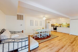A bedroom with a bed, a dining table with chairs, a kitchen area, and a ceiling fan.