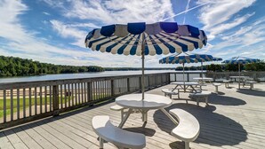 A deck with picnic tables and blue-striped umbrellas overlooking a lake.