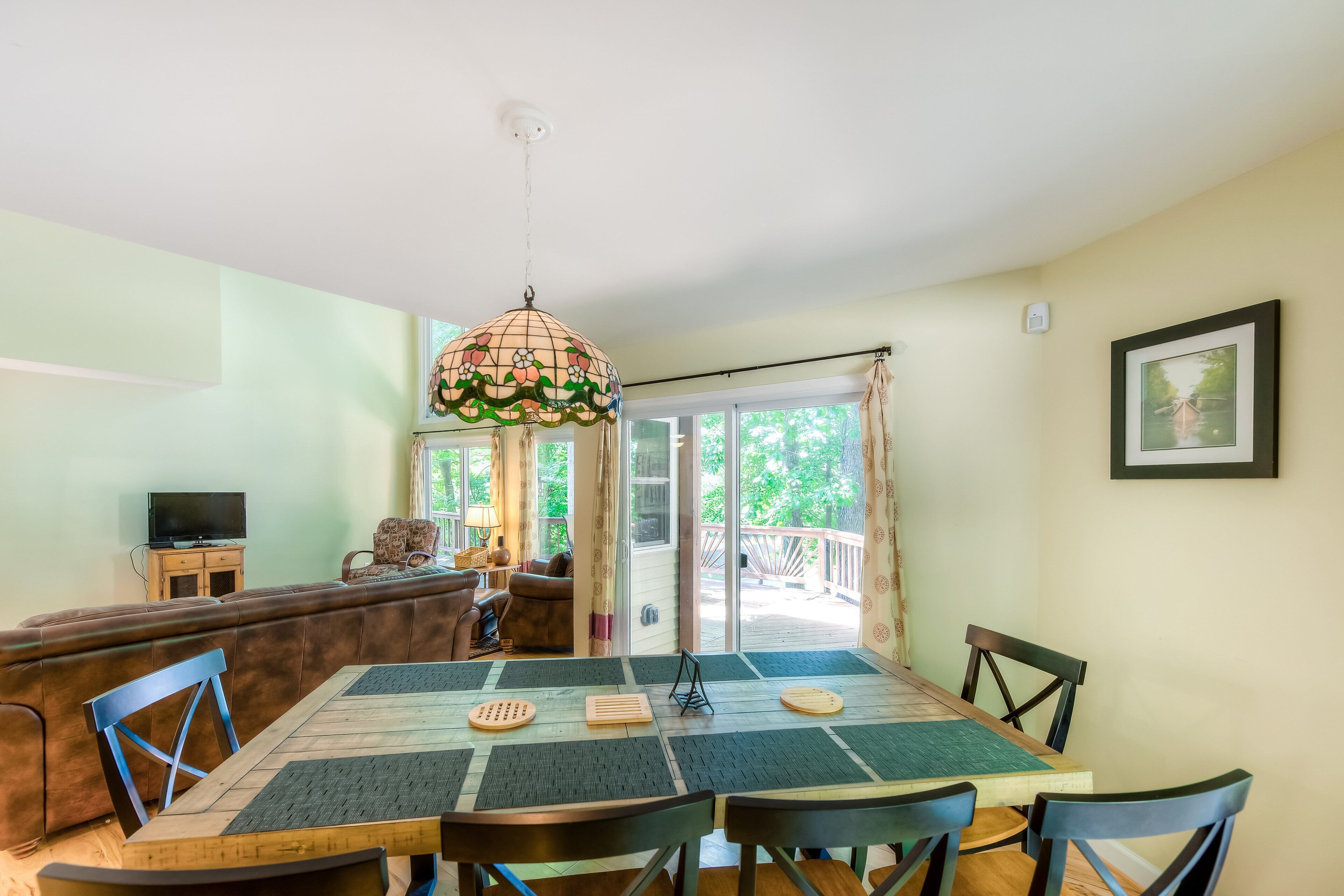 A dining area with a table, chairs, a sofa, a television, and a balcony with a view.