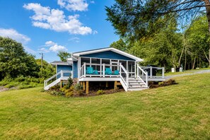 Ein zweistöckiges Haus mit Terrasse, Treppe und Sitzgelegenheiten im Freien.
