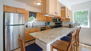 A kitchen with wooden cabinets, stainless steel appliances, a granite countertop, and a large island with bar stools. - Spacious pet Friendly Waterfront House With Patio & Grill (Bumpass)