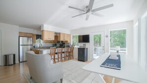 A modern kitchen with wooden cabinets, a stainless steel refrigerator, and a dining area with a white table and chairs. - Spacious pet Friendly Waterfront House With Patio & Grill (Bumpass)