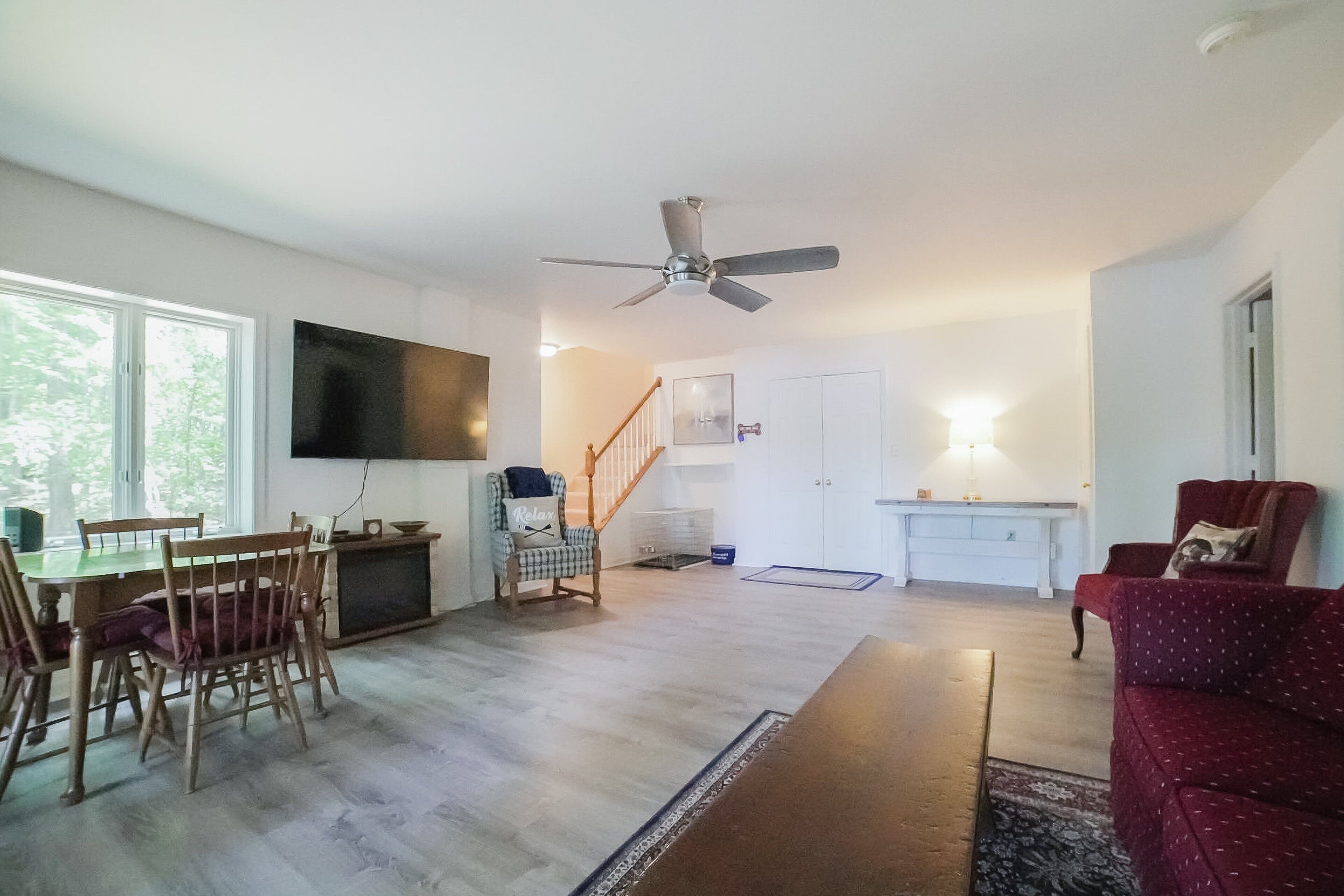 A spacious living room with a dining area, a ceiling fan, and a staircase leading to another level.