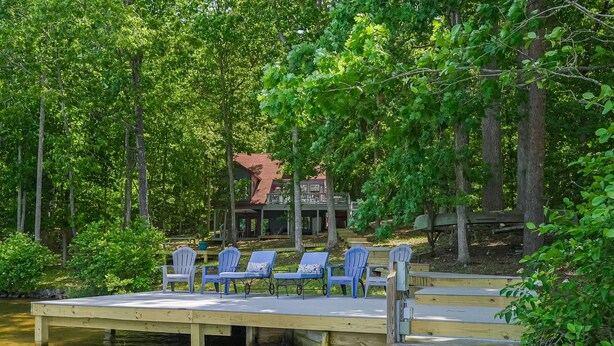 A dock with chairs, a building with a red roof, and a forested area. - Spacious pet Friendly Waterfront House With Patio & Grill (Bumpass)