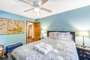 A bedroom with a bed, two bedside lamps, a ceiling fan, a wooden door, and a wall painting. - Lakefront Retreat With Dock, Private Hot Tub, Central AC, and Private Beach (Bumpass)