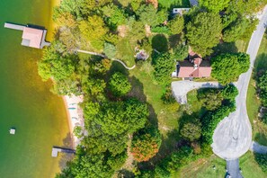An aerial view of a lakeside property with a dock, a pathway, and a house with a red roof. - Lakefront Retreat With Dock, Private Hot Tub, Central AC, and Private Beach (Bumpass)