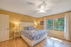 A bedroom with a bed, a nightstand, a ceiling fan, a window with a view, and a door. - Lakefront Family Home in Gated Community With Swimming Area & Dock - Dogs OK (Bumpass)