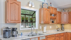 Una cocina con gabinetes de madera, encimera de granito, cafetera, tostadora y ventana con plantas en macetas.