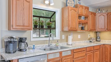 A kitchen with wooden cabinets, a granite countertop, a coffee maker, a toaster, and a window with potted plants.