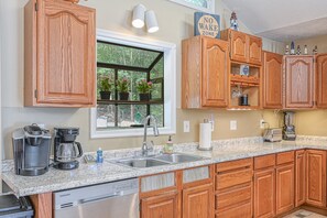 A kitchen with wooden cabinets, a granite countertop, a coffee maker, a toaster, and a window with potted plants. - Lakefront Family Home in Gated Community With Swimming Area & Dock - Dogs OK (Bumpass)