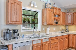 Una cocina con gabinetes de madera, encimera de granito, cafetera, tostadora y ventana con plantas en macetas.