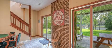 A room with a pool table, a 'NO WAKE ZONE' sign, a wooden chair, and a view of a backyard with a picnic table.