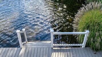 A wooden dock extending over water with a railing and a small vent.