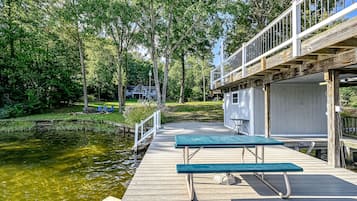 A wooden dock extending over a pond with picnic tables and a covered area with a railing.