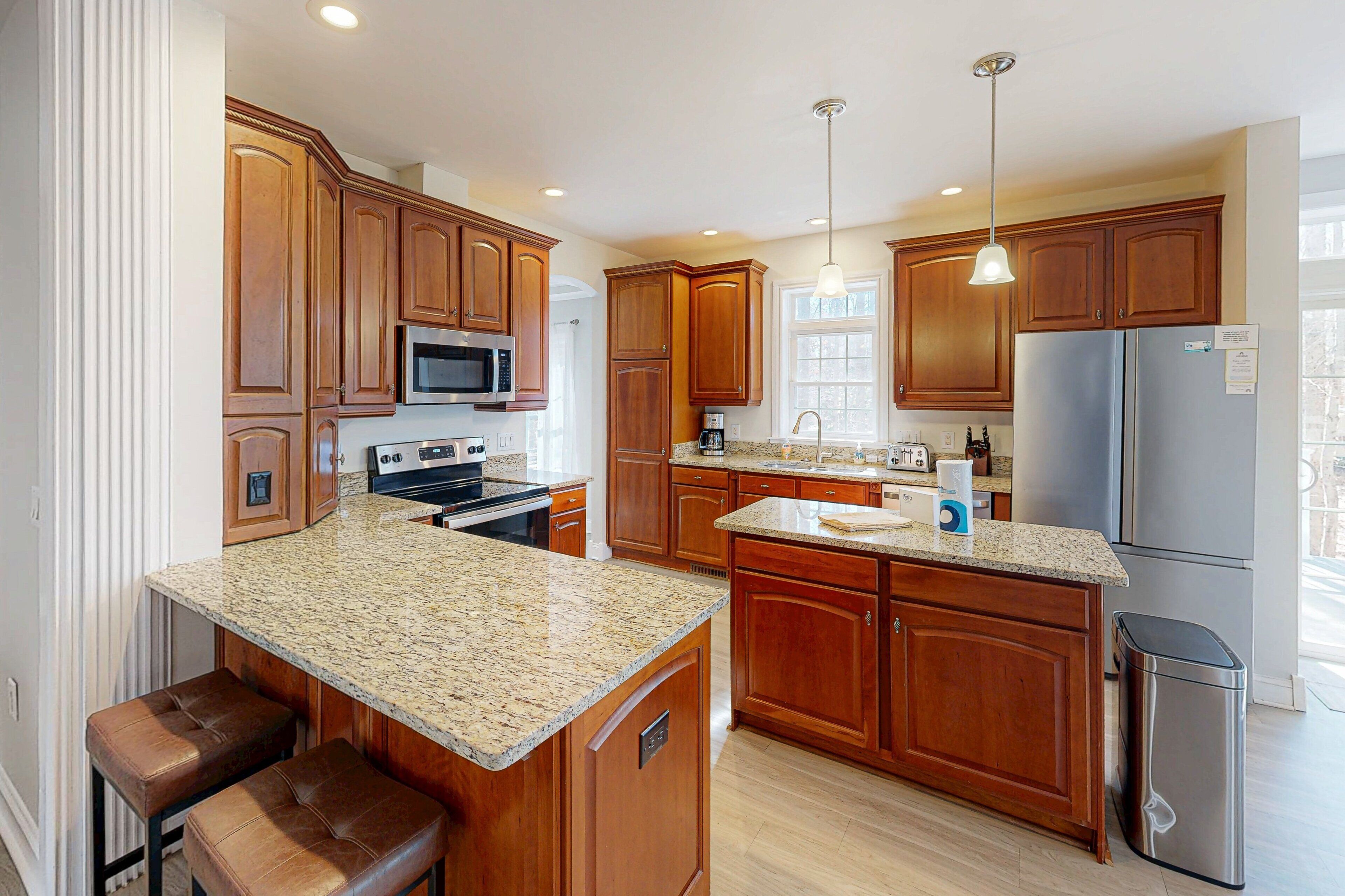 A kitchen with wooden cabinets, granite countertops, stainless steel appliances, and a trash can.