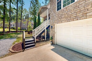 A residential house with a stone exterior, a white garage door, and a staircase leading to a covered porch. - Family-friendly Waterfront Retreat With Game Room, EV Charger, & More! (Bumpass)