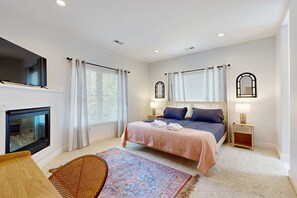 A bedroom with a bed, bedside lamps, a television, a fireplace, and a patterned rug. - Family-friendly Waterfront Retreat With Game Room, EV Charger, & More! (Bumpass)