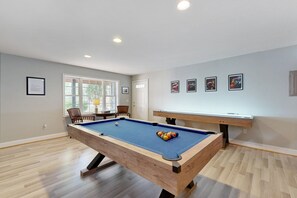 A pool table with a blue felt surface, a wooden table with a light-colored tabletop, and a wall with framed pictures. - Family-friendly Waterfront Retreat With Game Room, EV Charger, & More! (Bumpass)