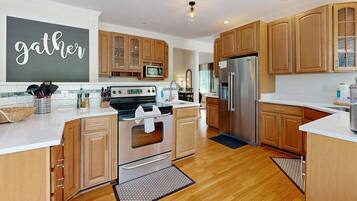 A modern kitchen with wooden cabinets, stainless steel appliances, and a 'gather' sign on the wall.