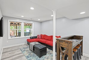 A room with a red sectional sofa, a black ottoman, a wooden coffee table, and a patterned rug. - Lakefront Home With Boat Mooring, Deck, hot Tub, Game Room & Fast Wifi - Dogs OK (Bumpass)