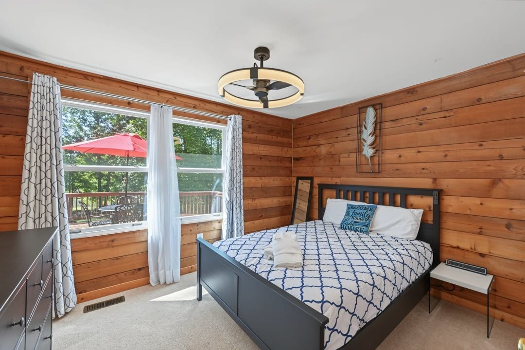 A bedroom with a bed, a bedside table, a ceiling fan, and a window with curtains.