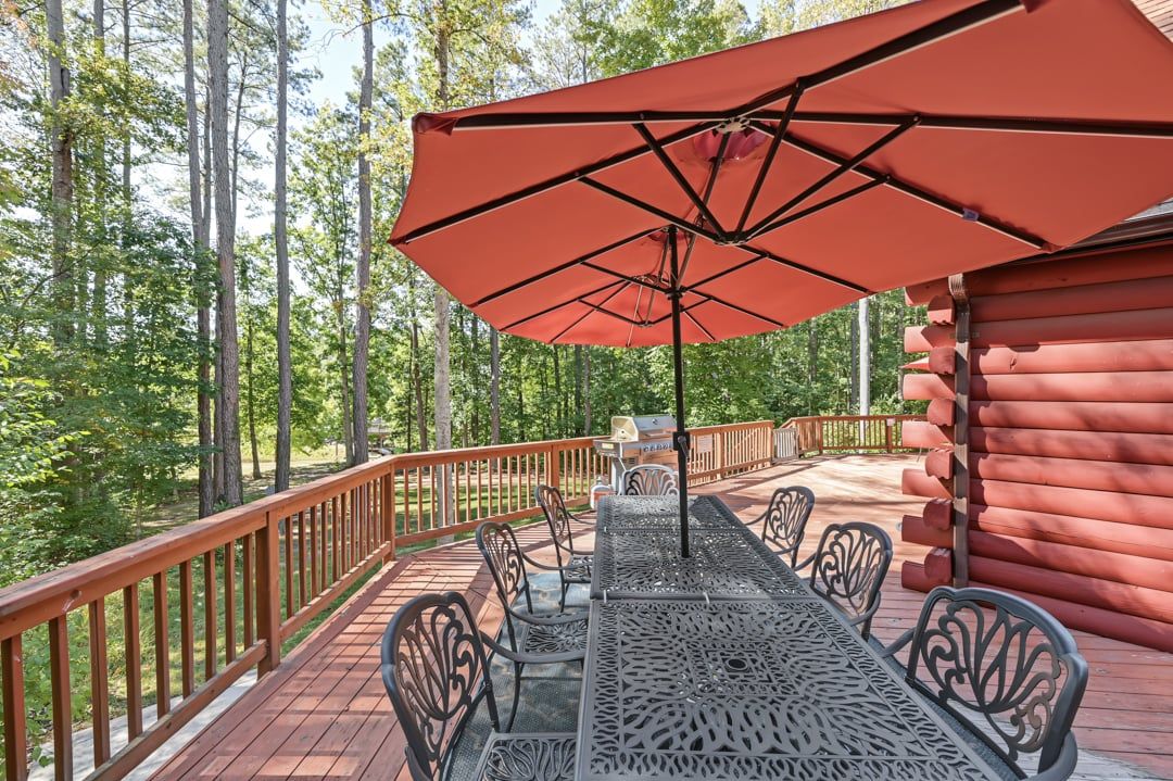 A deck with a table and chairs, a red umbrella, and a wooden cabin in a forest.